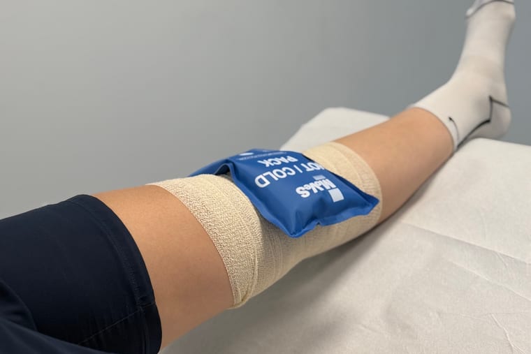 Hlajenje operiranega kolena z gelnim obkladkom, noga je dvignjena in povita